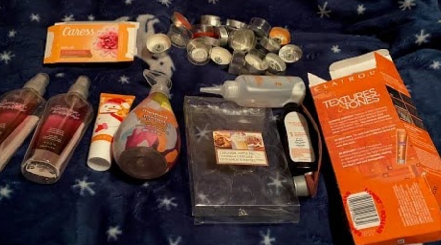 An illustrative image depicting empty product containers on a dark blanket includes a Caress soap bar box, used tealight candles, a Clairol Textures and Tones box with the dye and conditioner bottles, an empty tealights package, a bottle with a soap pump for Method hand soap, an empty tube of Avon hand cream, and two spray bottles that once had body spray from Avon as part of my empties project, or Project Pan.