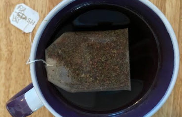 A cup of tea steeping in a white and purple mug.