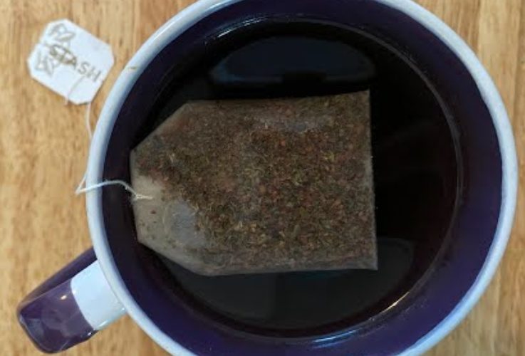 A cup of tea steeping in a white and purple mug.