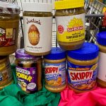 Jars of peanut and other nut butters sit in the seat of a shopping cart, stacked on top of each other.