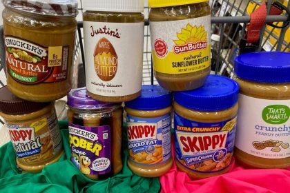 Jars of peanut and other nut butters sit in the seat of a shopping cart, stacked on top of each other.