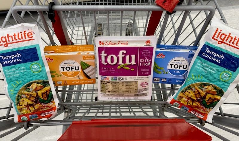 Packages of tofu sit in a grocery cart seat, with a package of tempeh on the far left and right sides.