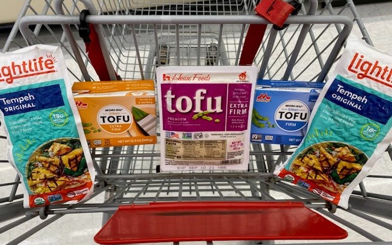 Packages of tofu sit in a grocery cart seat, with a package of tempeh on the far left and right sides.