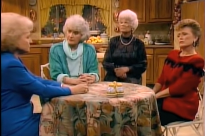 A decorative image screenshot of an episode of The Golden Girls, with Betty White as Rose Nylund wearing a blue suit, Estelle Getty as Sophia Petrillo wearing a turquoise cardigan and a light blue sweater, Bea Arthur as Dorothy Zbornak wearing a black sweater and a gold necklace, Rue McClanahan as Blanche Deveraux wearing a red and black striped sweater, all sitting at the kitchen table, covered in a floral-print tablecloth.