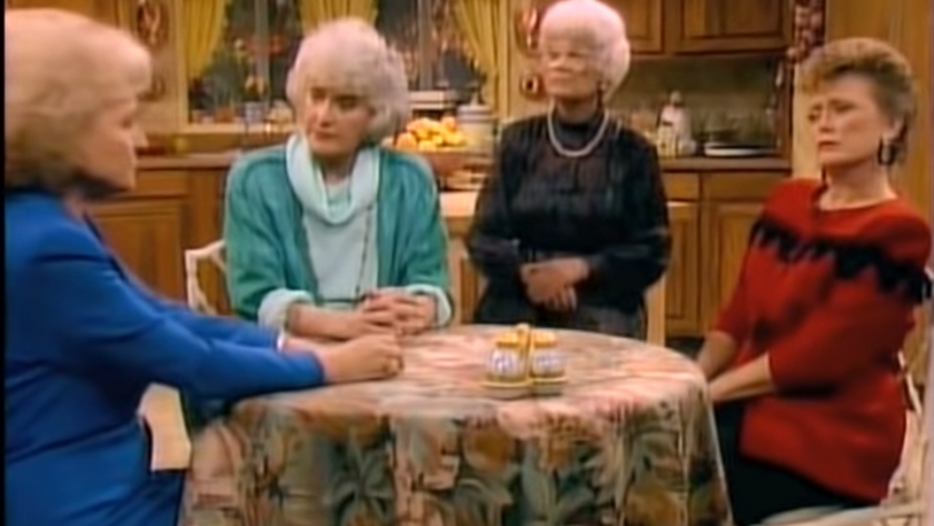 A decorative image screenshot of an episode of The Golden Girls, with Betty White as Rose Nylund wearing a blue suit, Estelle Getty as Sophia Petrillo wearing a turquoise cardigan and a light blue sweater, Bea Arthur as Dorothy Zbornak wearing a black sweater and a gold necklace, Rue McClanahan as Blanche Deveraux wearing a red and black striped sweater, all sitting at the kitchen table, covered in a floral-print tablecloth.