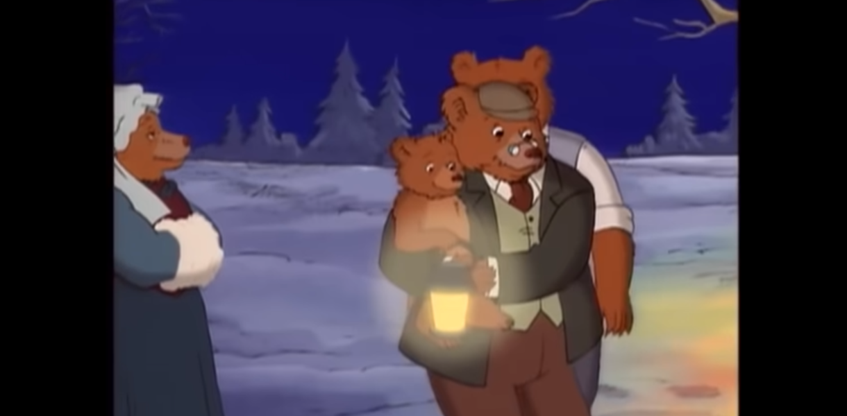 A screenshot from an episode of Little Bear, about their winter solstice celebration. Little Bear is in Grandpa Bear's arms, holding a lantern to hang on the tree for the snow angels. Grandma Bear is on the left hand side. Grandma Bear is wearing an 1890s dress and a bonnet. Grandpa Bear wears a dress shirt, tie, pants, and a vest in the style of the 1890s.