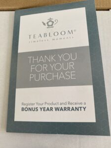 A close up of a piece of literature included in the box the Buckingham Palace teapot set came in, and text reads: Teabloom Timeless Moments. Thank you for your purchase. Register your product and receive a bonus year warranty.