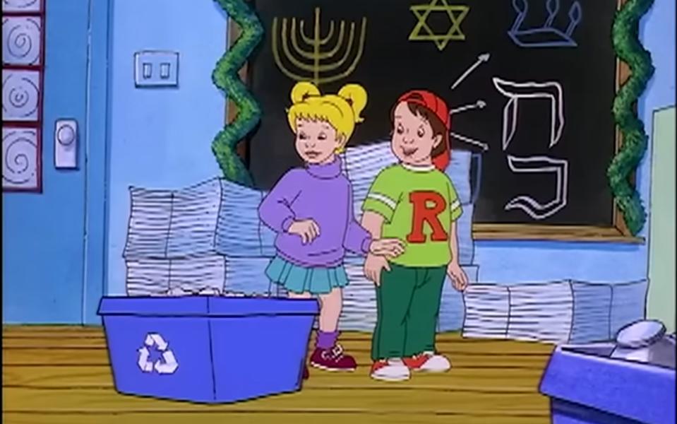 Screenshot from a holiday episode of The Magic School Bus, w/ Dorothy Ann and Ralph standing in front of a chalkboard decorated w/ menorahs and the Star of David. Dorothy Ann and Ralph are standing next to blue recycling bins.