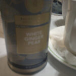 A photo of a canister of White Ginger Pear tea from Teabloom, sitting on a white marble-hued coffee table, next to an old white mug full of tea.